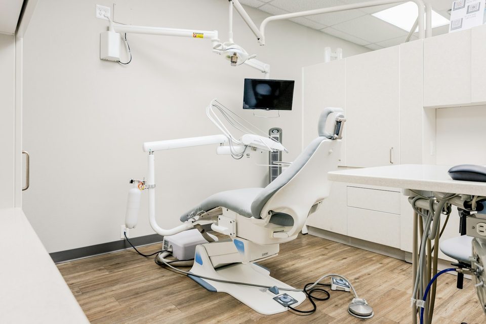Sala de atendimento clínico com cadeira laranja, equipamentos e janela iluminada